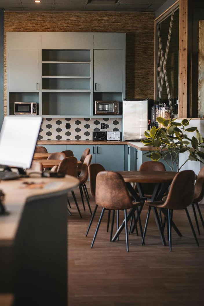 A modern office breakroom with seating, a kitchenette, and a plant